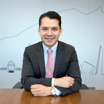 Persona con traje oscuro y corbata rosa sonriendo.