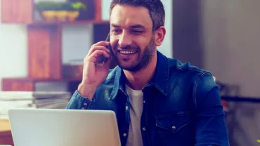 Persona hablando por teléfono mientras usa una computadora portátil.
