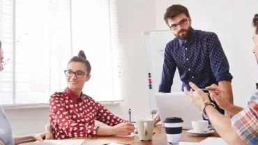 Grupo de personas en una reunión de trabajo con una pizarra y portátiles.