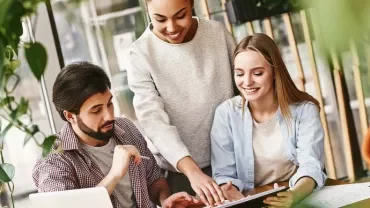 Tres personas colaboran en un proyecto en una mesa de oficina.