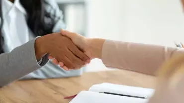 Dos personas dándose la mano sobre una mesa de oficina.