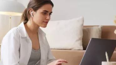 Mujer con audífonos frente a una computadora 