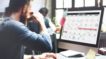 Persona trabajando en un escritorio con un calendario en la pantalla de la computadora.