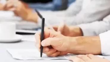 Personas escribiendo en una reunión, con tazas y computadoras portátiles en una mesa.