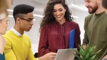 Grupo de personas trabajando en equipo con laptop y plantas.