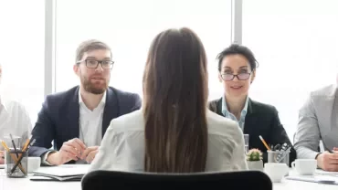 Una persona de espaldas en una entrevista con cuatro personas sentadas en la mesa.