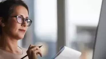 Persona leyendo notas frente a una computadora en oficina.
