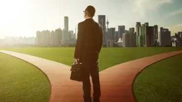 Persona de pie en una bifurcación de caminos con una ciudad al fondo.