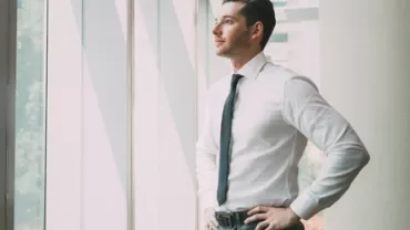 Persona de pie junto a una ventana con luz natural.