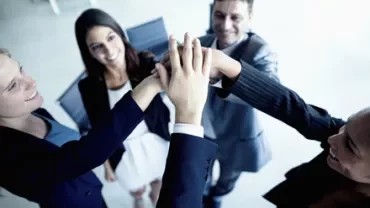 Personas uniendo sus manos en el centro en un gesto de trabajo en equipo.