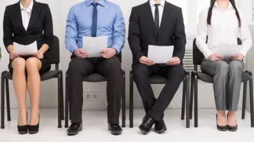 Cuatro personas sentadas en fila, cada una con un documento en mano.