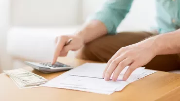 Persona usando calculadora y revisando facturas en una mesa.