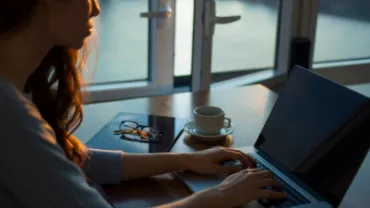 Persona trabajando en una computadora portátil junto a una ventana.