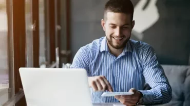 Persona sonriendo mientras usa una laptop y una tablet en una cafetería.