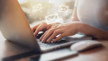 Persona escribiendo en una laptop con iconos de correo flotando.