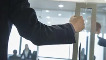 Persona abriendo una puerta de cristal en una oficina.