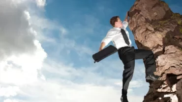 Persona escalando una roca con traje formal y maletín.