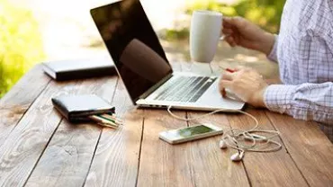 Persona utilizando una laptop sobre una mesa de madera al aire libre.