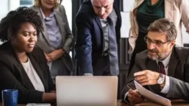 Grupo de personas discutiendo frente a una computadora portátil.