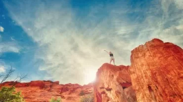 Persona en lo alto de un acantilado bajo un cielo azul.