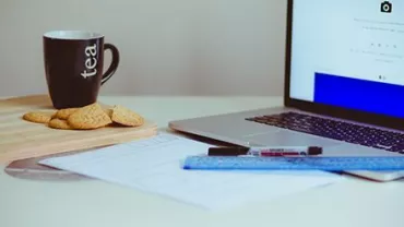 Taza de té y galletas junto a una computadora portátil en un escritorio.