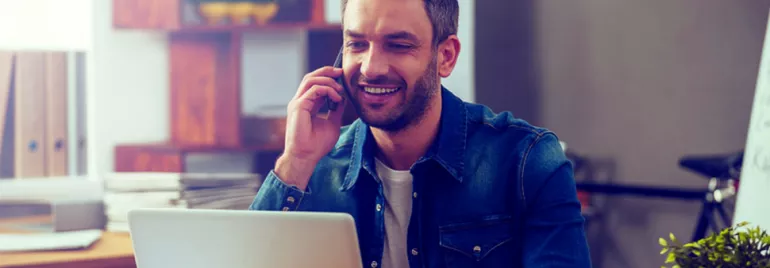 Persona hablando por teléfono mientras usa una computadora portátil.