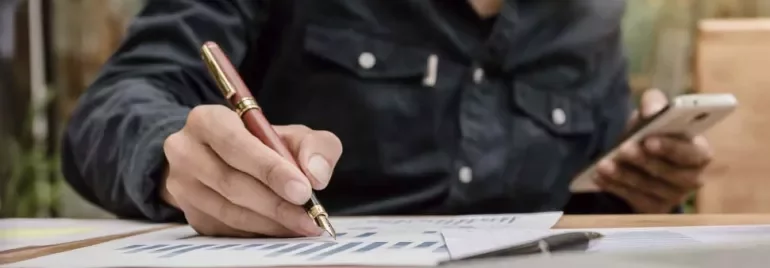 Persona escribiendo en gráficos con un bolígrafo y sosteniendo un teléfono.