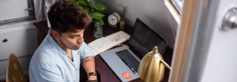 Persona escribiendo en un cuaderno junto a una computadora portátil.