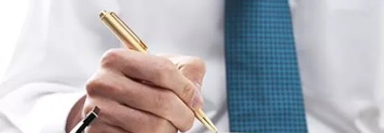 Persona escribiendo en una agenda con una pluma dorada.