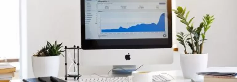Escritorio con ordenador mostrando gráfico de datos, rodeado de plantas y libros.