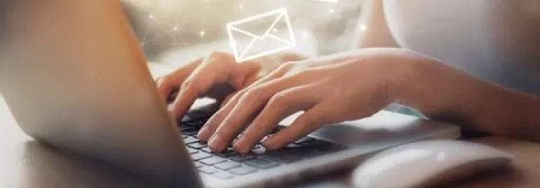 Persona escribiendo en una laptop con iconos de correo flotando.