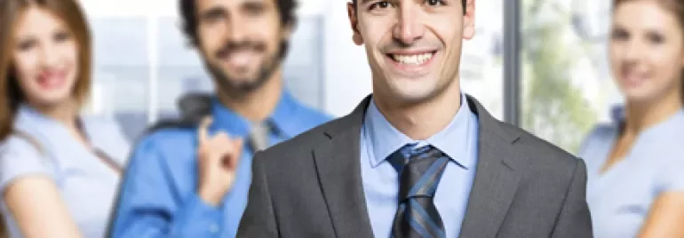 Persona sonriendo en traje, con grupo profesional atrás.