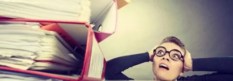 Persona sorprendida al ver una gran pila de carpetas y papeles.