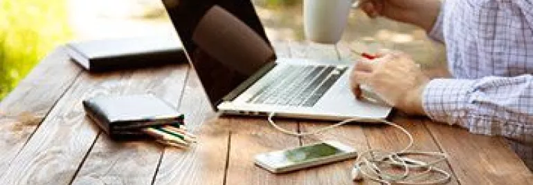 Persona utilizando una laptop sobre una mesa de madera al aire libre.