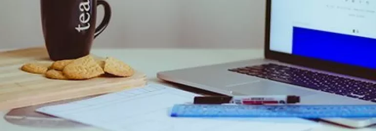 Taza de té y galletas junto a una computadora portátil en un escritorio.