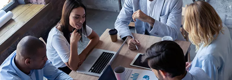 Grupo de personas trabajando en una oficina con laptops y gráficos.