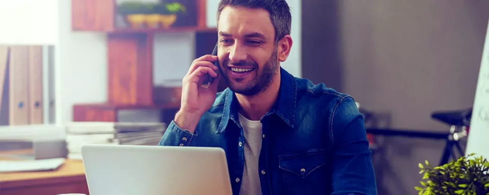 Persona hablando por teléfono mientras usa una computadora portátil.