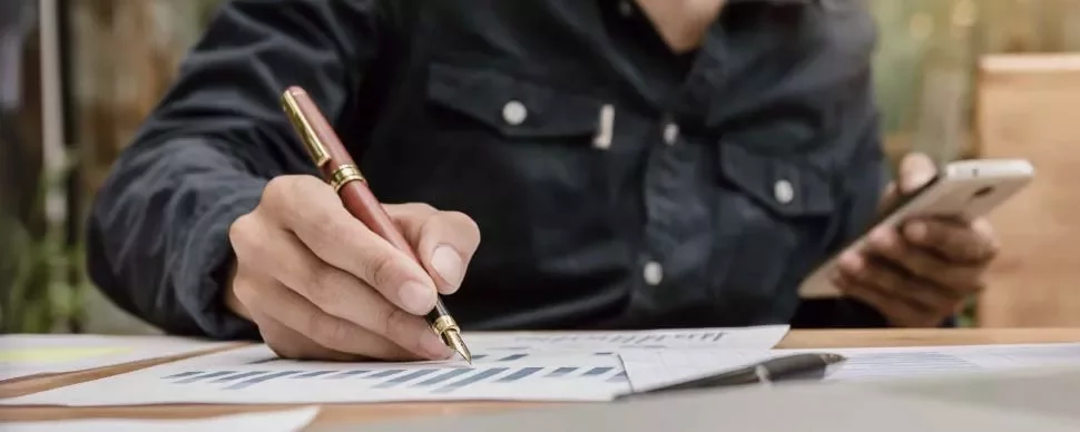 Persona escribiendo en gráficos con un bolígrafo y sosteniendo un teléfono.