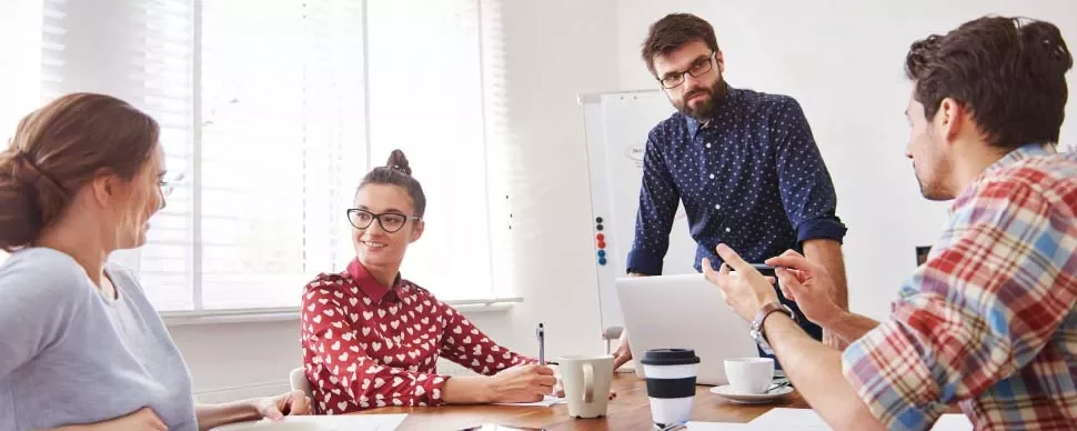 Grupo de personas en una reunión de trabajo con una pizarra y portátiles.