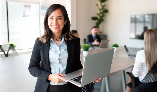 Persona sonriendo sosteniendo una laptop en una oficina moderna