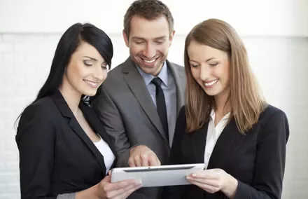 Personas en traje mirando una tableta con sonrisas.