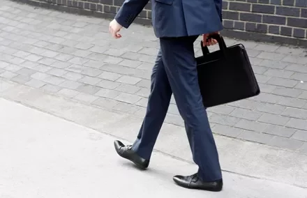 Persona caminando con traje azul y maletín negro.