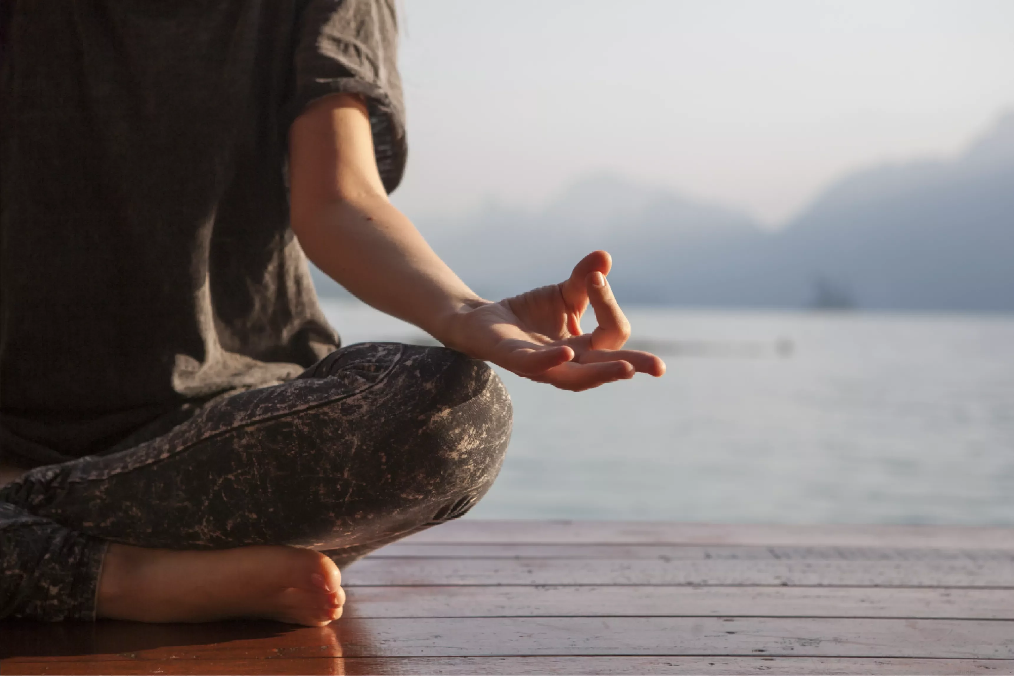 Persona meditando en posición de loto junto a un lago.