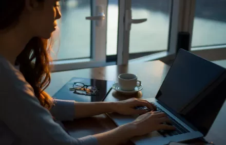 Persona trabajando en una computadora portátil junto a una ventana.