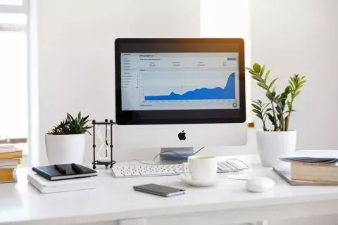Escritorio con ordenador mostrando gráfico de datos, rodeado de plantas y libros.