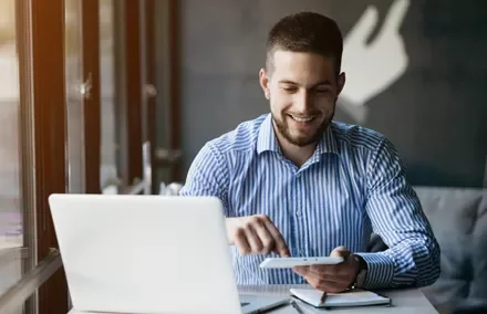Persona sonriendo mientras usa una laptop y una tablet en una cafetería.