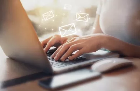 Persona escribiendo en una laptop con iconos de correo flotando.