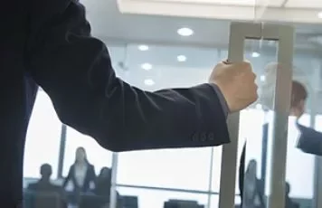 Persona abriendo una puerta de cristal en una oficina.