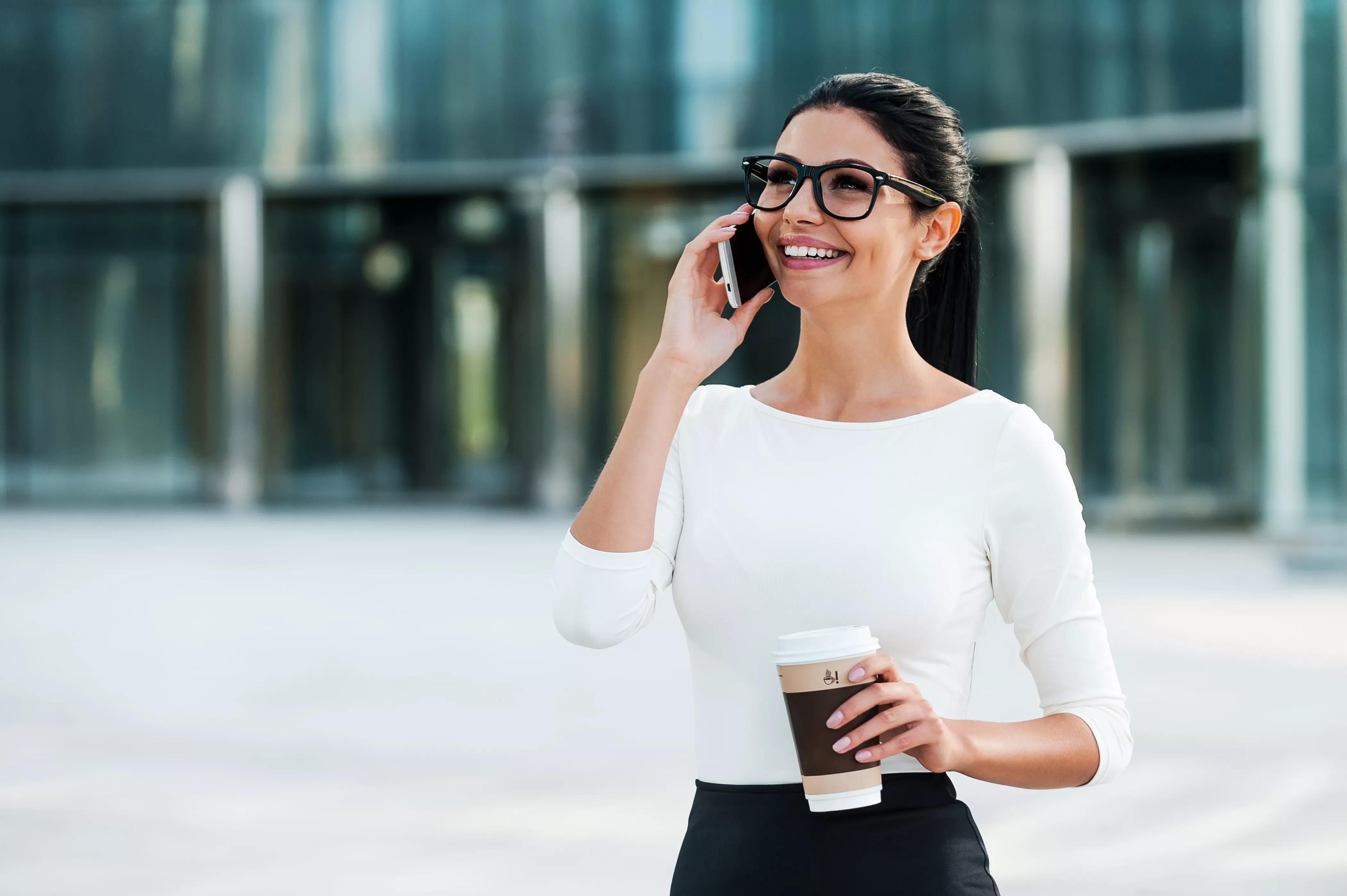 Persona sonriendo mientras habla por teléfono y sostiene un café.