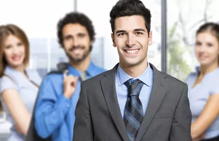 Persona sonriendo en traje, con grupo profesional atrás.